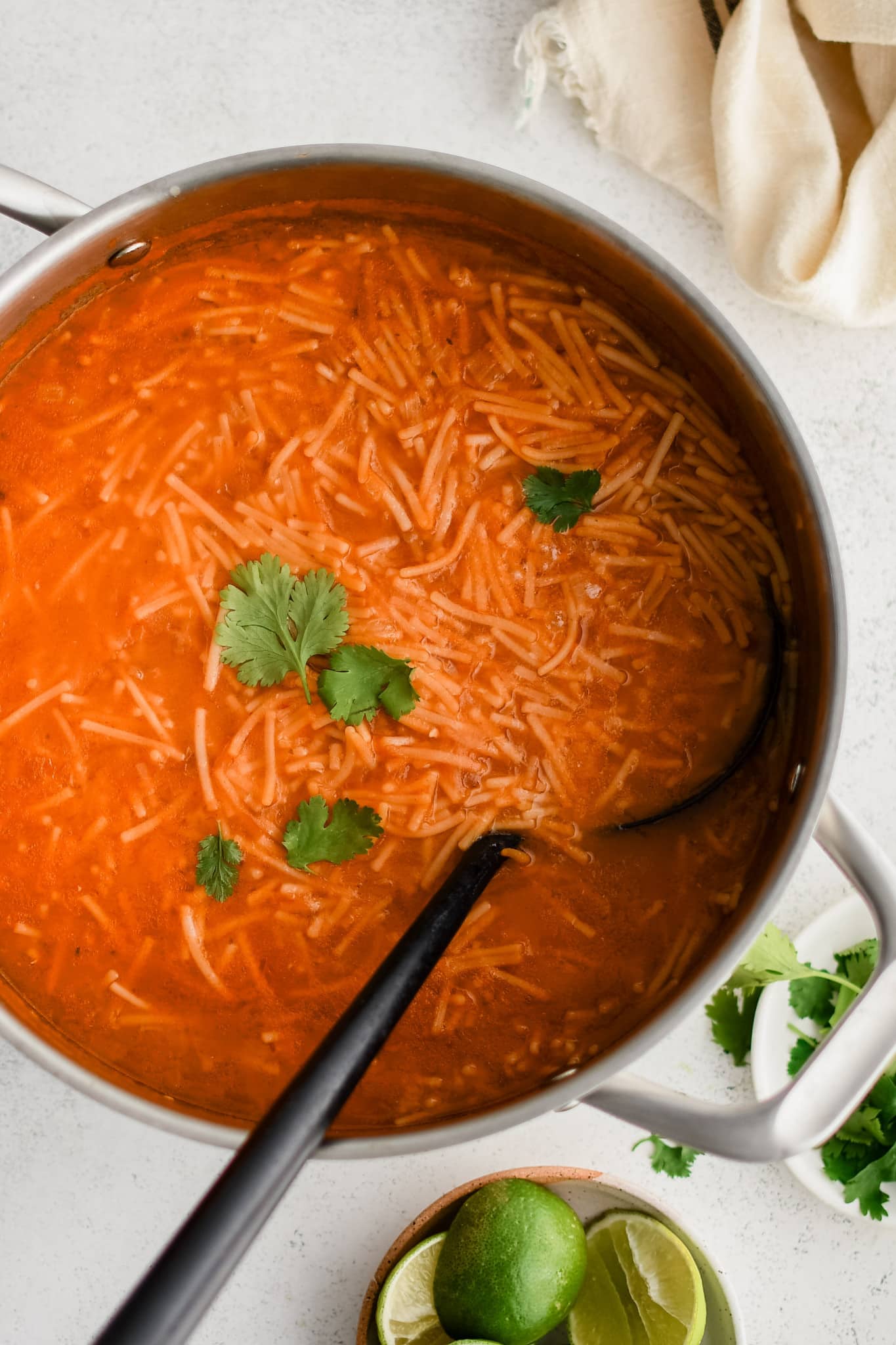 A black soup ladle in a soup pot filled with homemade sopa de fideo garnished with fresh cilantro.
