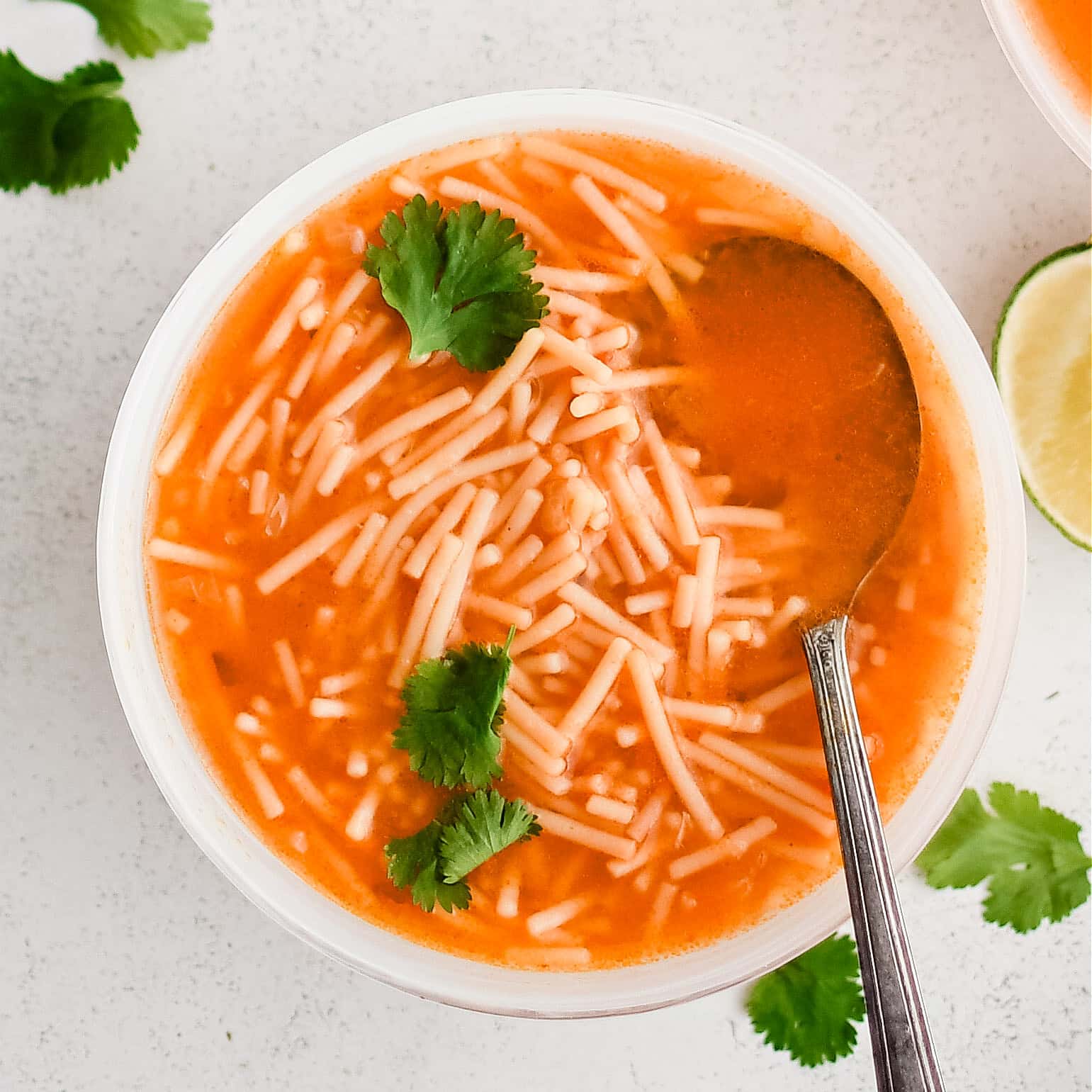 White soup bowl filled with Sopa De Fideo (Mexican Noodle Soup) made with a light tomato broth and small fideo noodles.