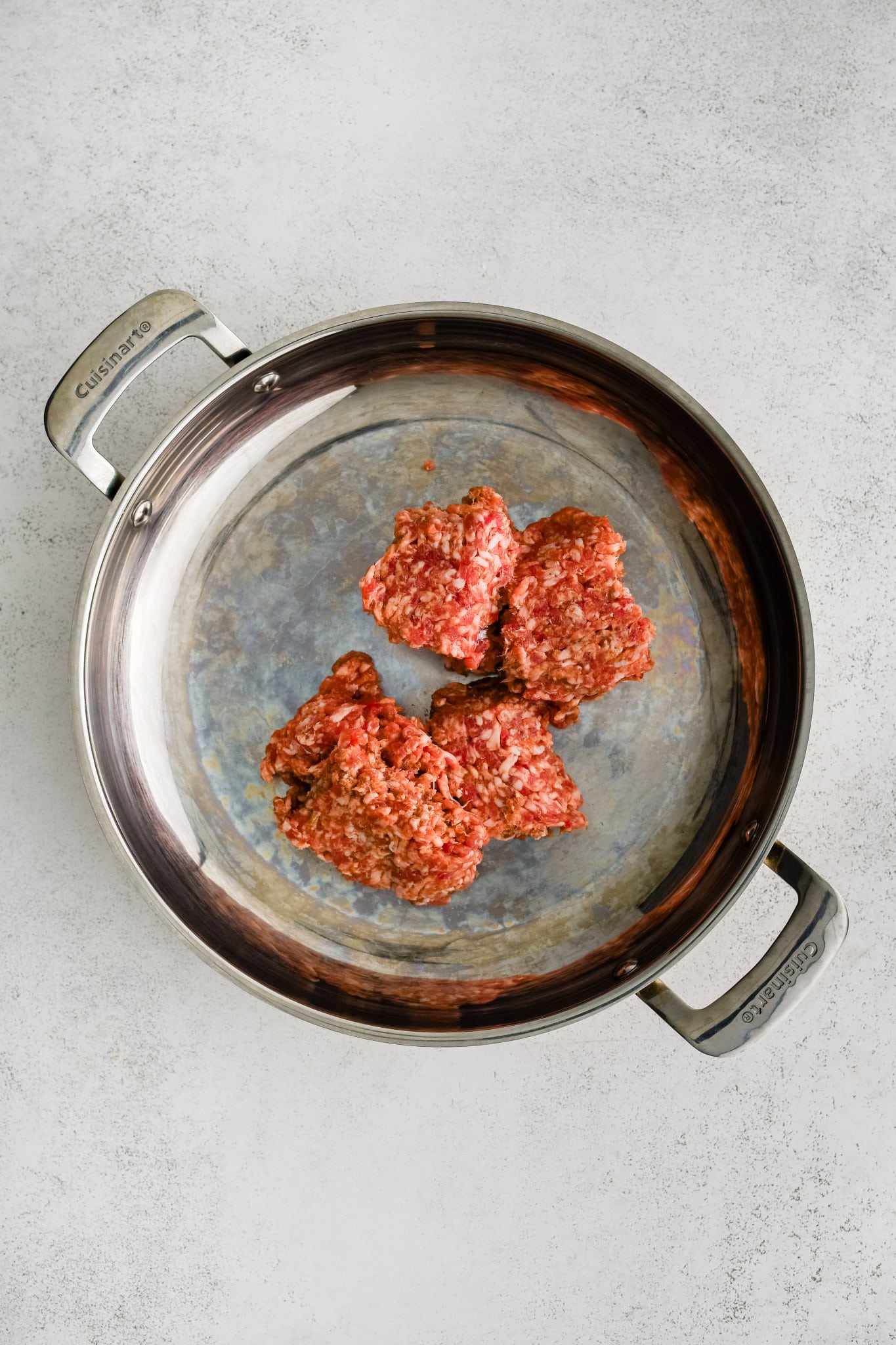 A large oven-safe skillet with raw ground Italian sausage.