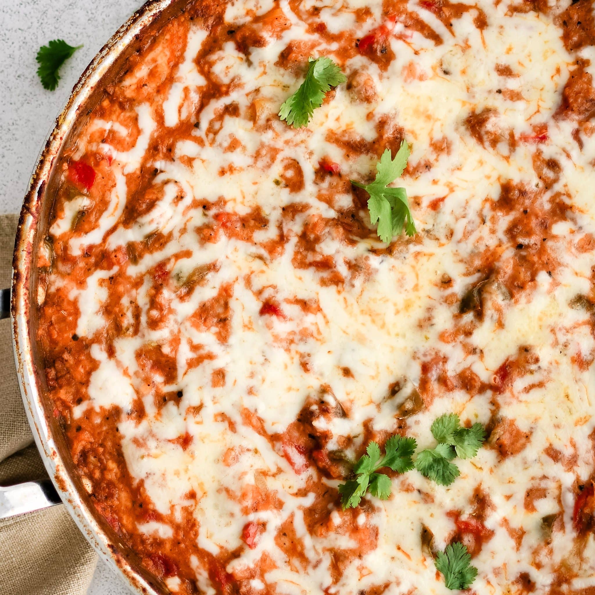 Large oven-safe skillet filled with Stuffed Pepper Casserole hot out of the oven and topped with gooey melted Monterey Jack cheese and garnished with fresh cilantro.