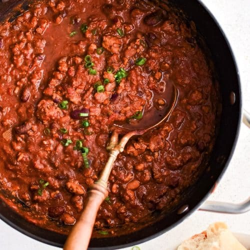 Large pot filled with simmering turkey chili with kidney and pinto beans and garnished with chopped green onions.