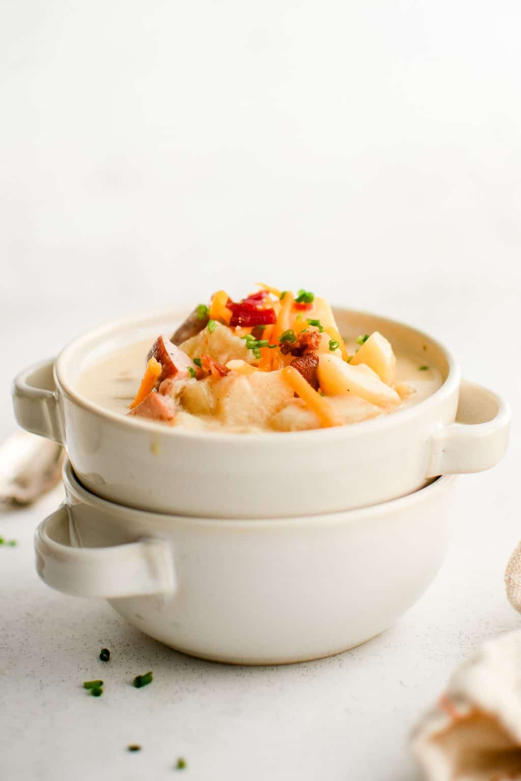 ham and potato soup in stacked white bowls with cheddar bacon chives