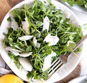 Crisp white plate topped with fresh arugula and shaved parmesan cheese with a light lemon vinaigrette.