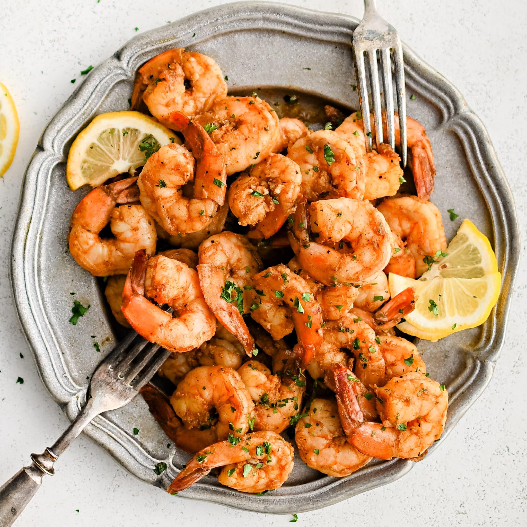 Large silver platter filled with well-seasoned Cajun shrimp garnished with chopped parsley and served with sliced lemon.