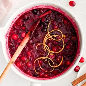 Medium saucepan filled with homemade cranberry sauce made with fresh cranberries and garnished with thin ribbons of orange peel.