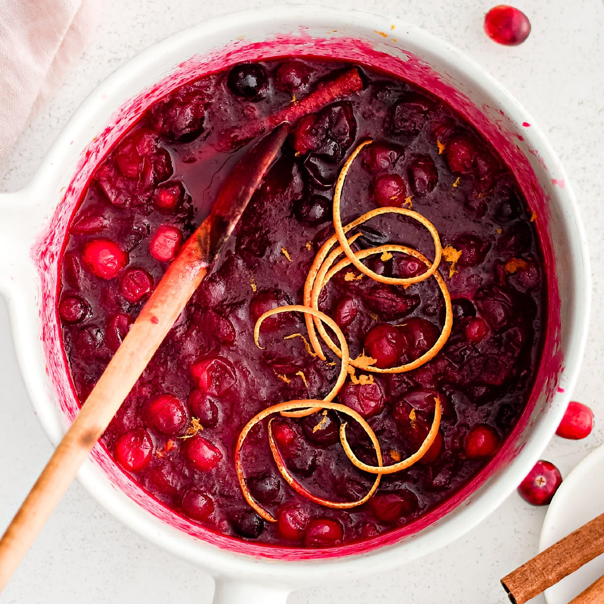 Medium saucepan filled with homemade cranberry sauce made with fresh cranberries and garnished with thin ribbons of orange peel.