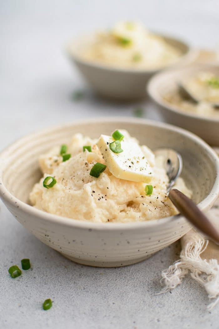 Several serving bowls filled with creamy, buttery mashed potatoes garnished with green onions.