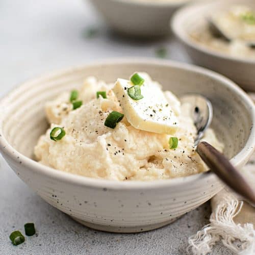 Several serving bowls filled with creamy, buttery mashed potatoes garnished with green onions.