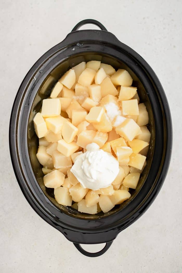 Butter, sour cream, and heavy cream added to peeled, diced, and cooked white potatoes in a large crockpot