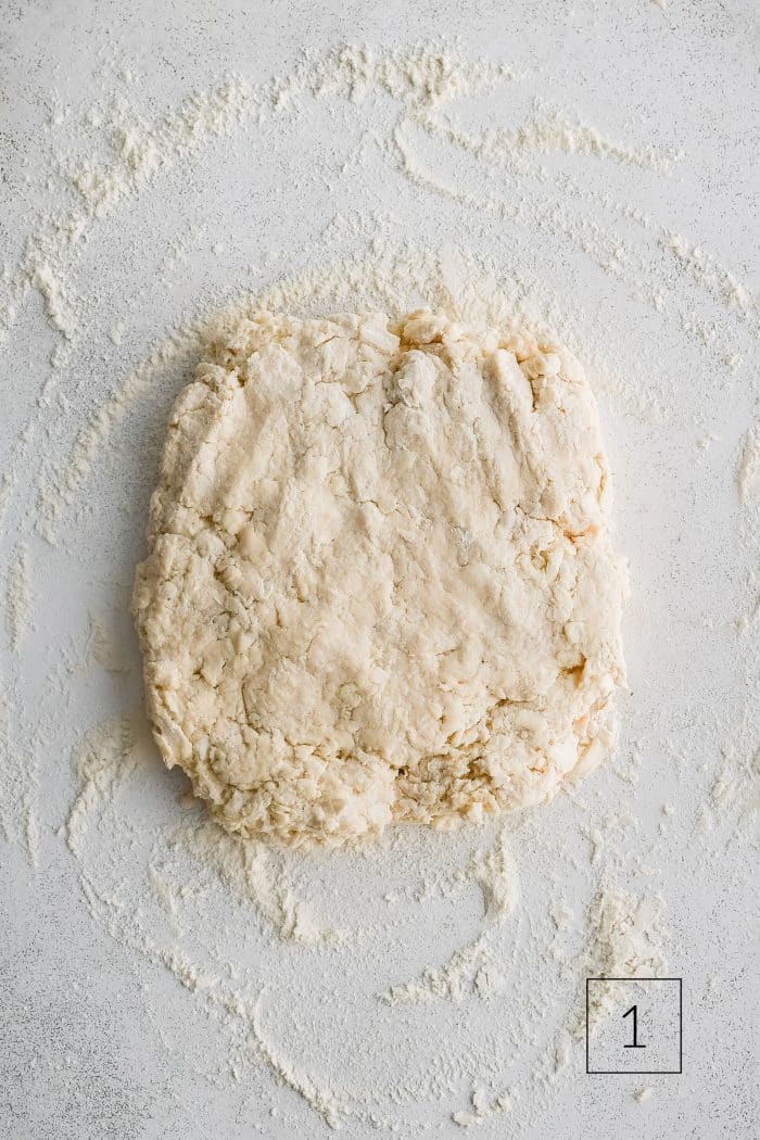 Buttermilk biscuit dough roughly shaped into a rectangle about 1/2-inch thick on a lightly floured work surface.