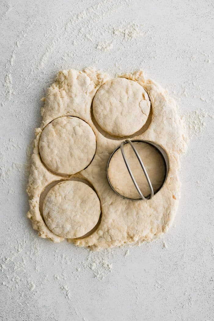 Four biscuits cut from homemade buttermilk biscuit dough roughly shaped into a rectangle about 1/2-inch thick on a lightly floured work surface.