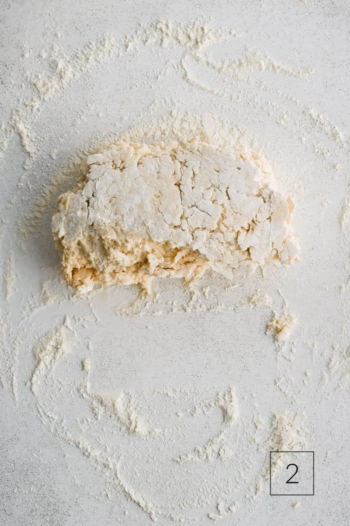 Buttermilk biscuit dough roughly shaped into a rectangle and folded in half on a lightly floured work surface.