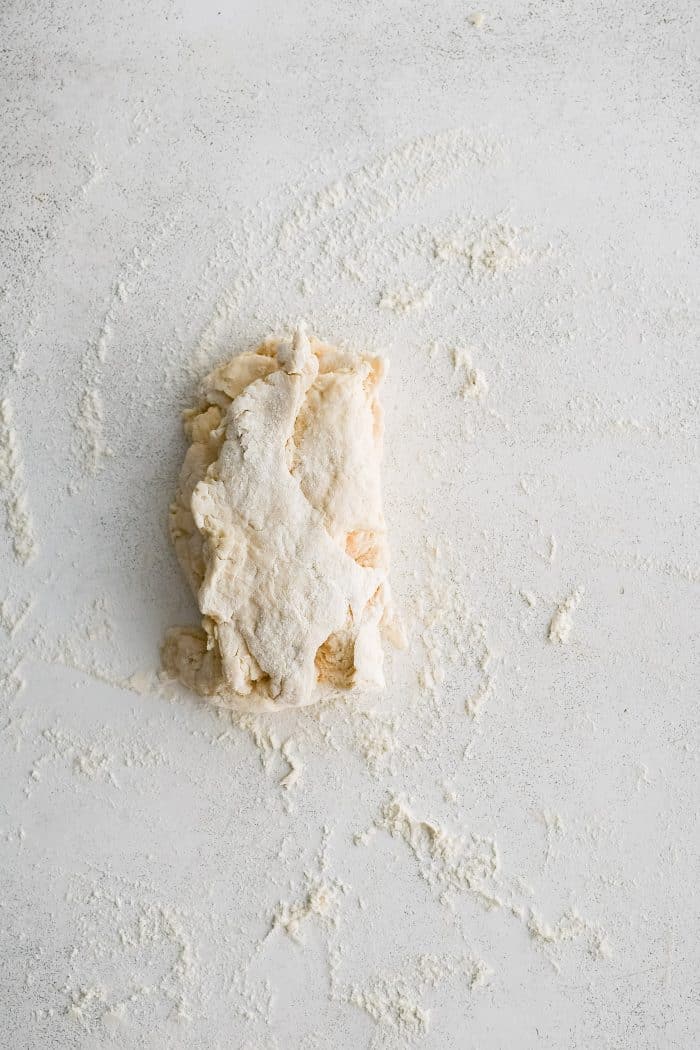 Buttermilk biscuit dough roughly shaped into a rectangle and folded in half on a lightly floured work surface.