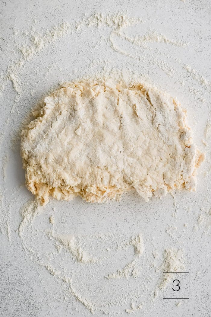 Buttermilk biscuit dough roughly shaped into a rectangle about 1/2-inch thick on a lightly floured work surface.