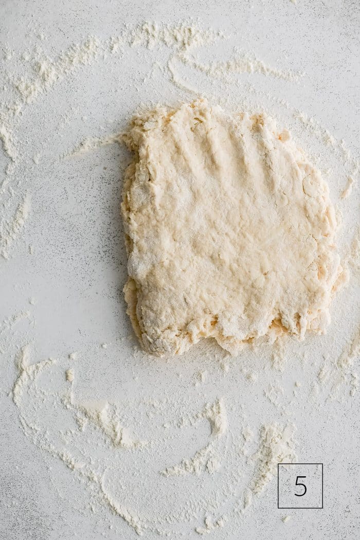 Buttermilk biscuit dough roughly shaped into a rectangle about 1/2-inch thick on a lightly floured work surface.