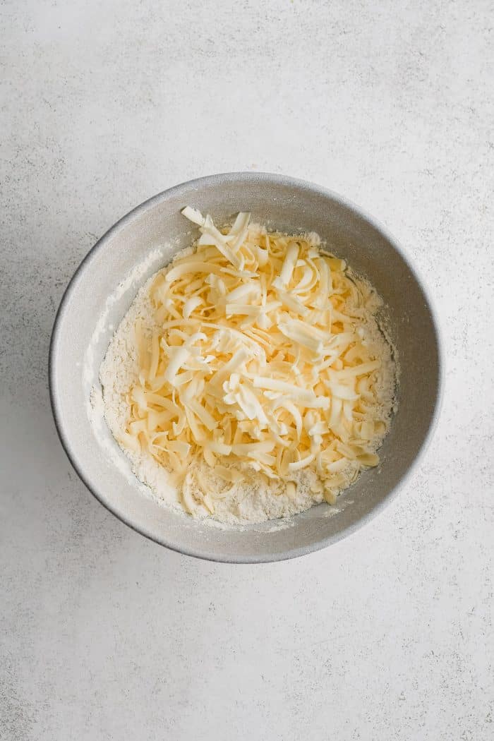 Large bowl with whisked together flour, baking powder, baking soda, and salt and cold shredded butter.