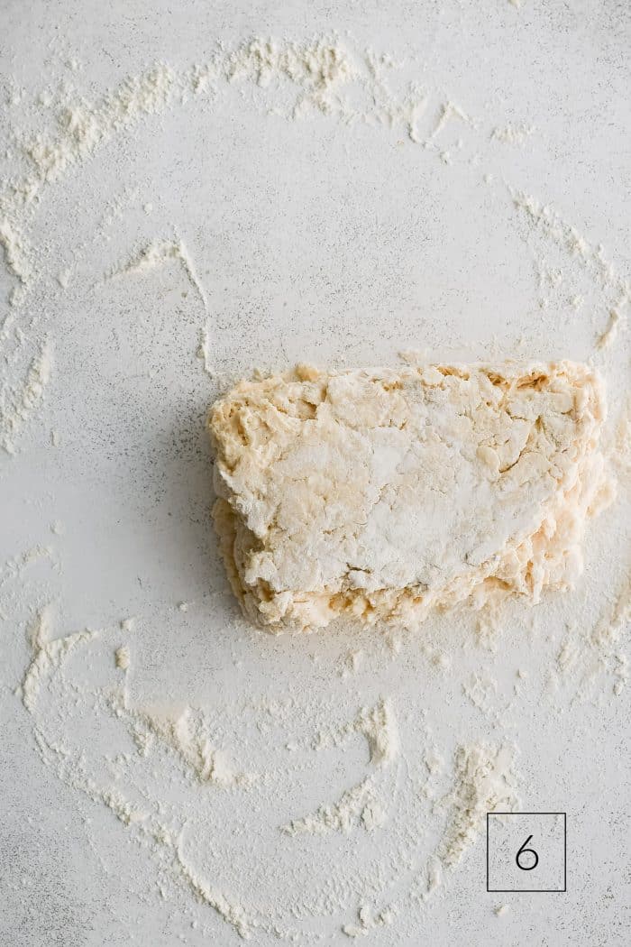 Buttermilk biscuit dough roughly shaped into a rectangle and folded in half on a lightly floured work surface.