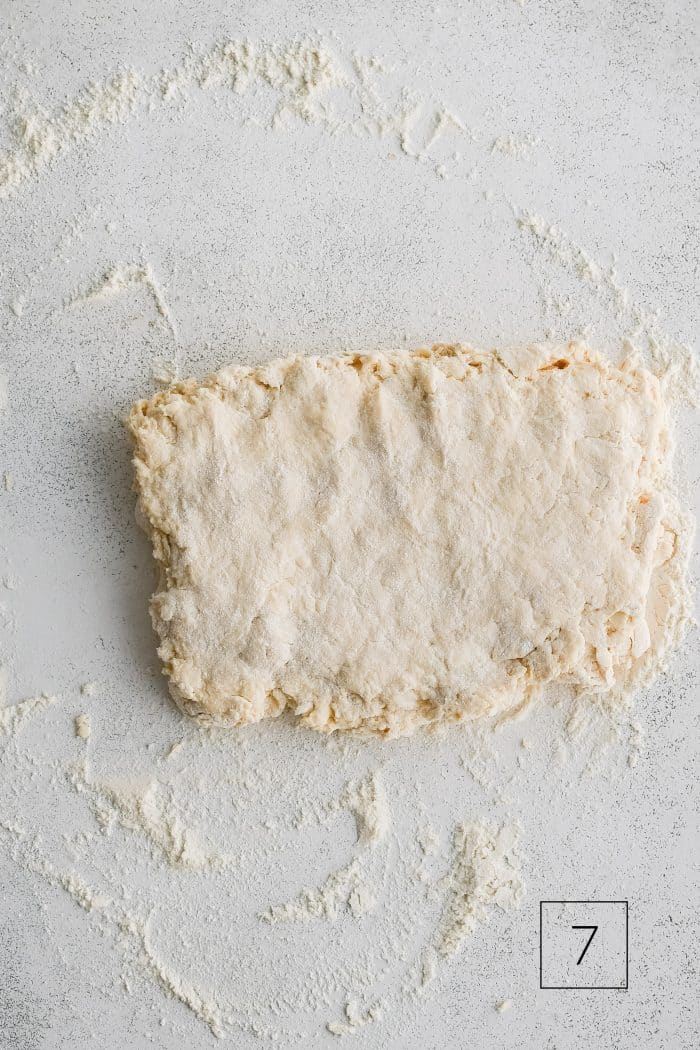 Buttermilk biscuit dough roughly shaped into a rectangle about 1/2-inch thick on a lightly floured work surface.