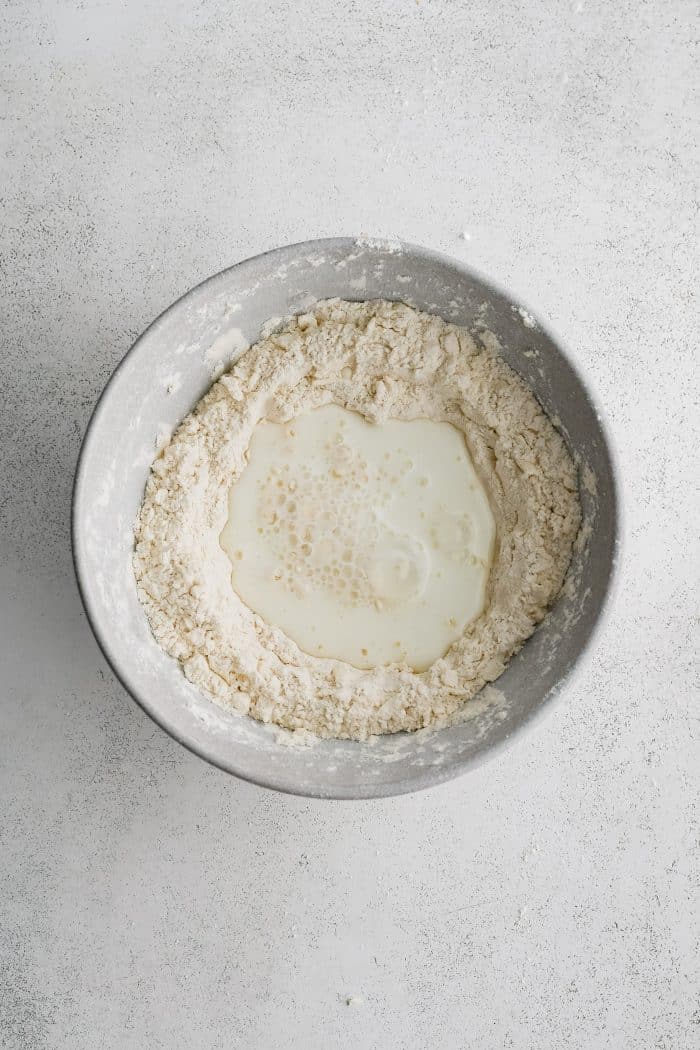 Buttermilk added to a large bowl filled with shredded butter mixed with a combination of flour, baking powder, baking soda, and salt.