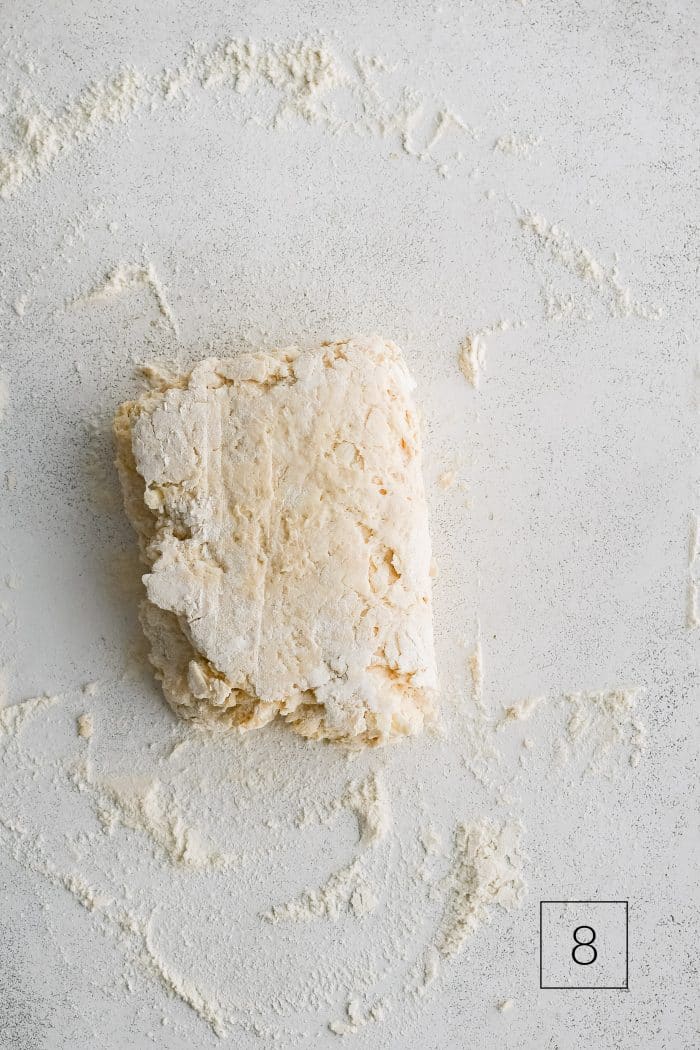 Buttermilk biscuit dough roughly shaped into a rectangle and folded in half on a lightly floured work surface.