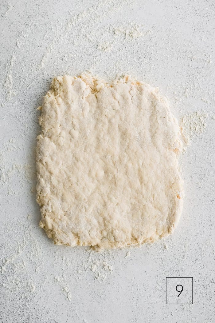 Buttermilk biscuit dough roughly shaped into a rectangle about 1/2-inch thick on a lightly floured work surface.