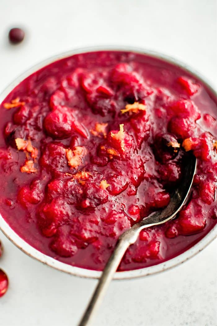 Large white bowl filled with homemade cranberry sauce garnished with fresh orange zest.