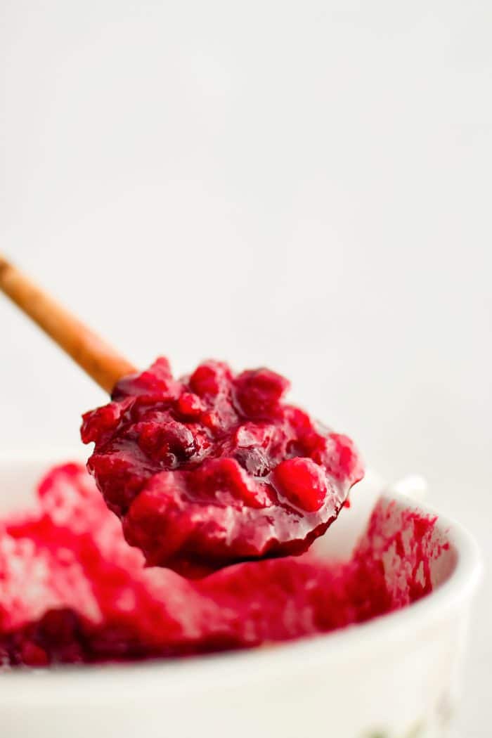 Large wooden spoon filled with homemade cranberry sauce made with whole fresh cranberries.