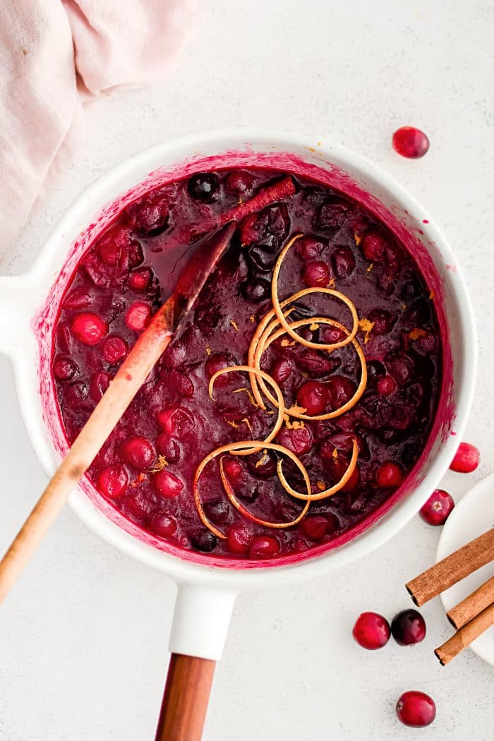 Medium saucepan filled with homemade cranberry sauce made with fresh cranberries and garnished with thin ribbons of orange peel.