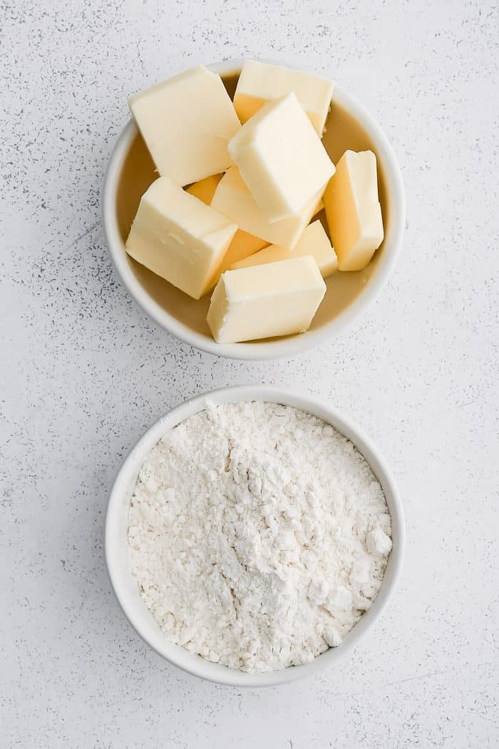 Two white bowls, one bowl filled with cubes of butter and the other bowl filled with all-purpose flour.