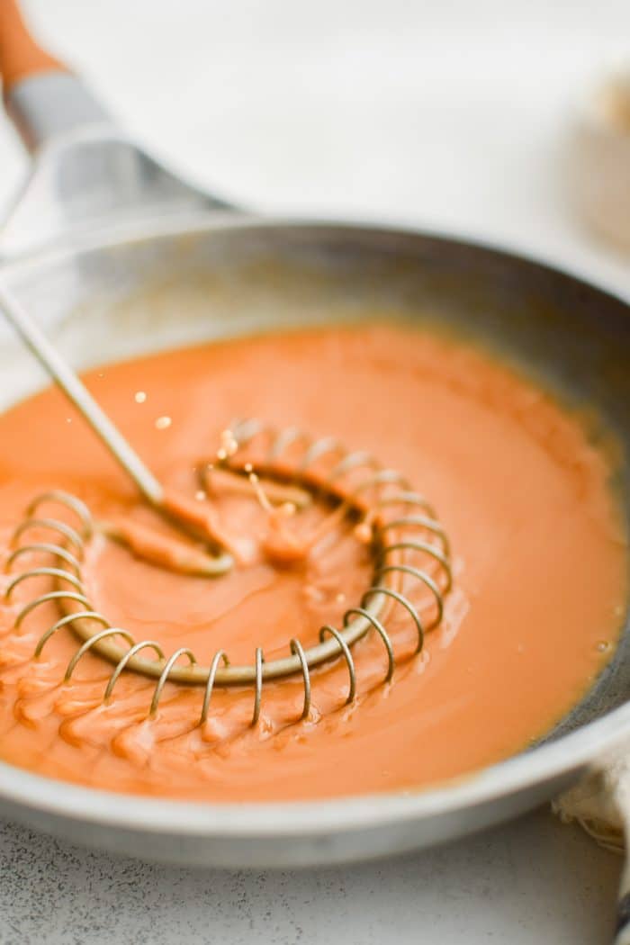 Sauce whisk set inside a skillet filled with brown roux.