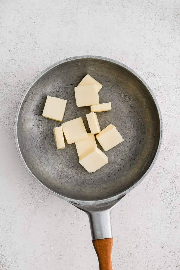 Pats of butter in a stainless steel skillet.