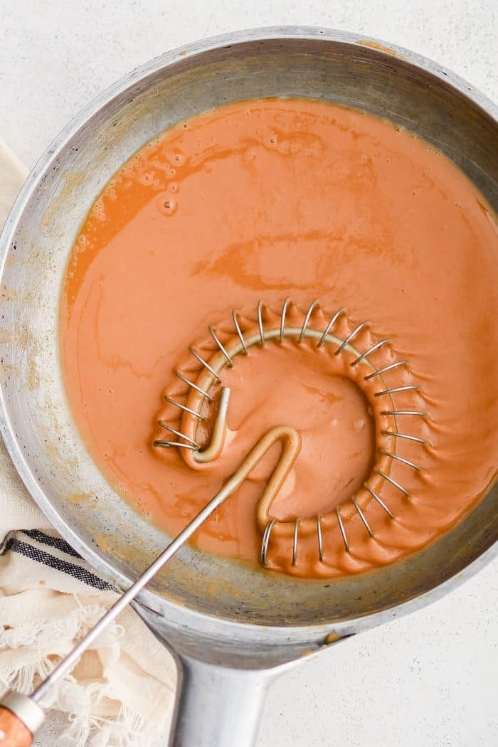 Sauce whisk set inside a skillet filled with dark brown roux.