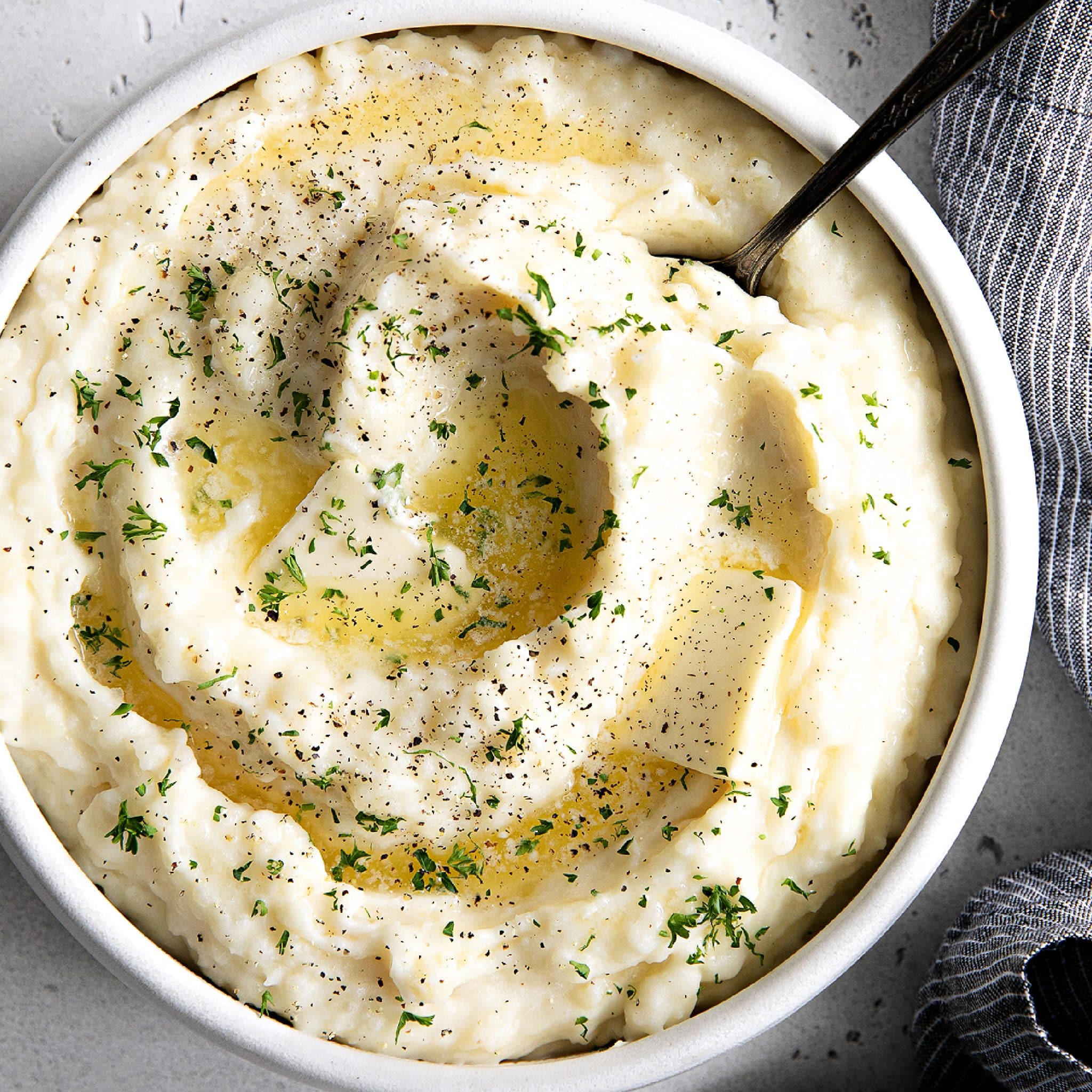 White bowl filled with creamy, rich, and fluffy mashed potatoes cooked in the Instant Pot and topped with melted butter and minced parsley.