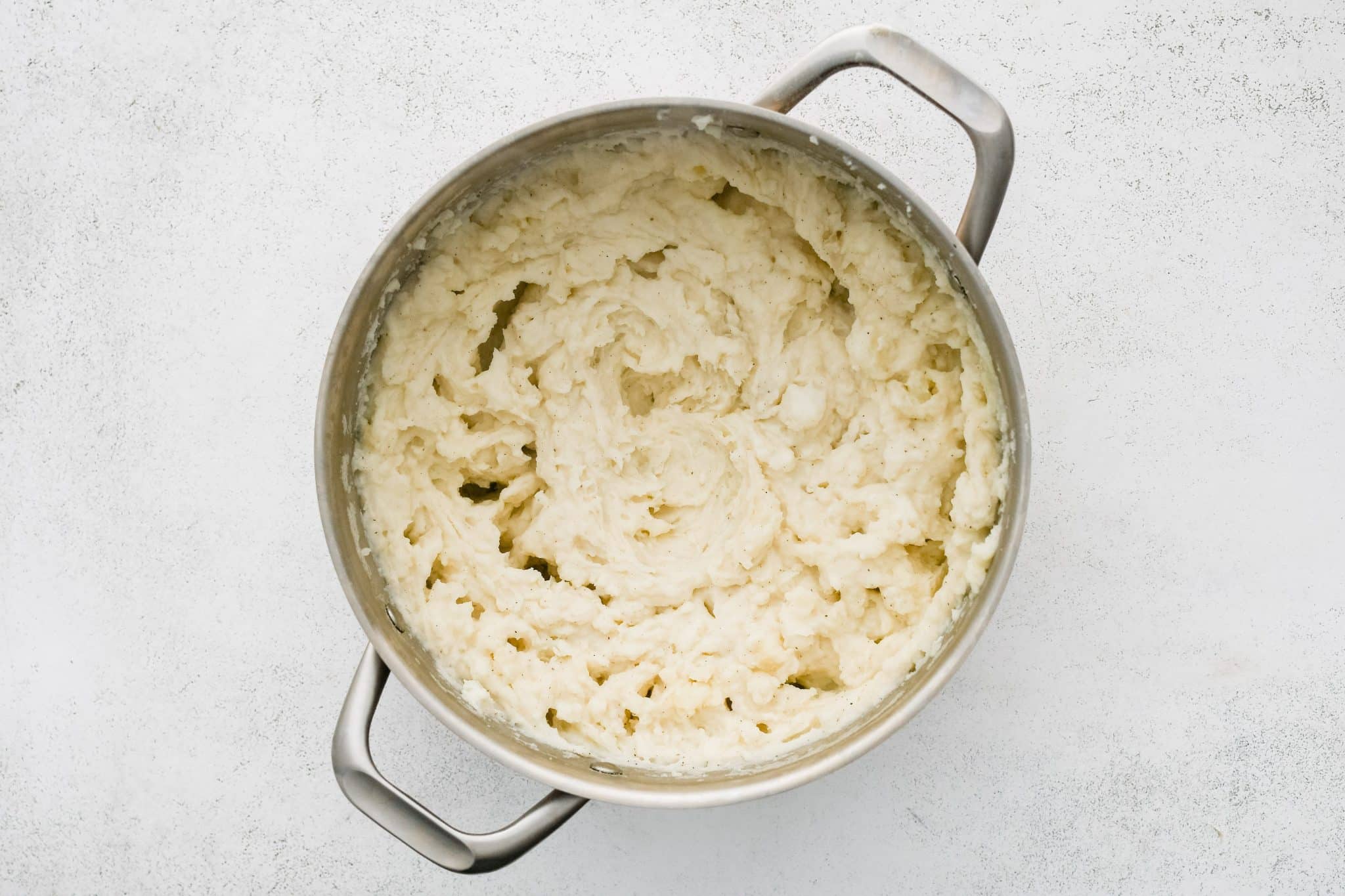 A large pot filled with creamy mashed russet potatoes flavored with salt, black pepper, sour cream, and heavy cream.