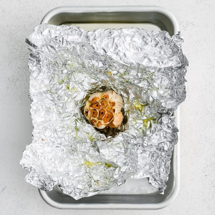 Whole bulb of roasted garlic with golden caramelized cloves on foil.