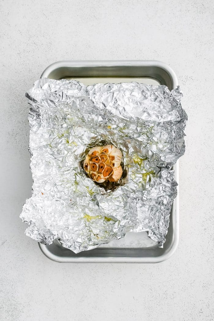 Whole bulb of roasted garlic with golden caramelized cloves on foil.