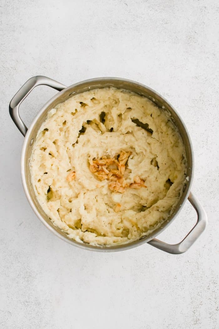 Whole cloves of roasted caramelized garlic added to a large pot filled with creamy mashed potatoes.