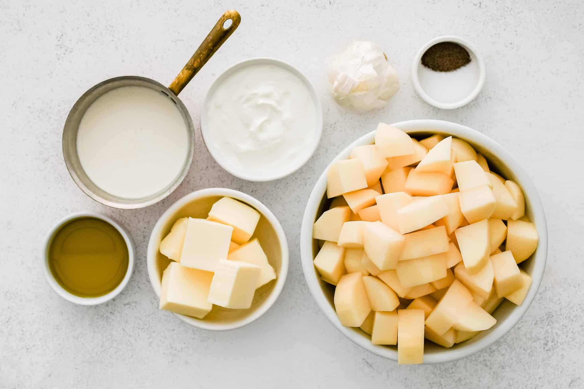 All of the ingredients needed to make roasted garlic mashed potatoes in individual measuring cups and ramekins.