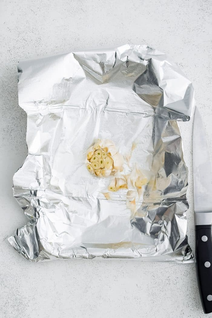 Whole garlic bulb on a piece of aluminum foil with the tip sliced off.