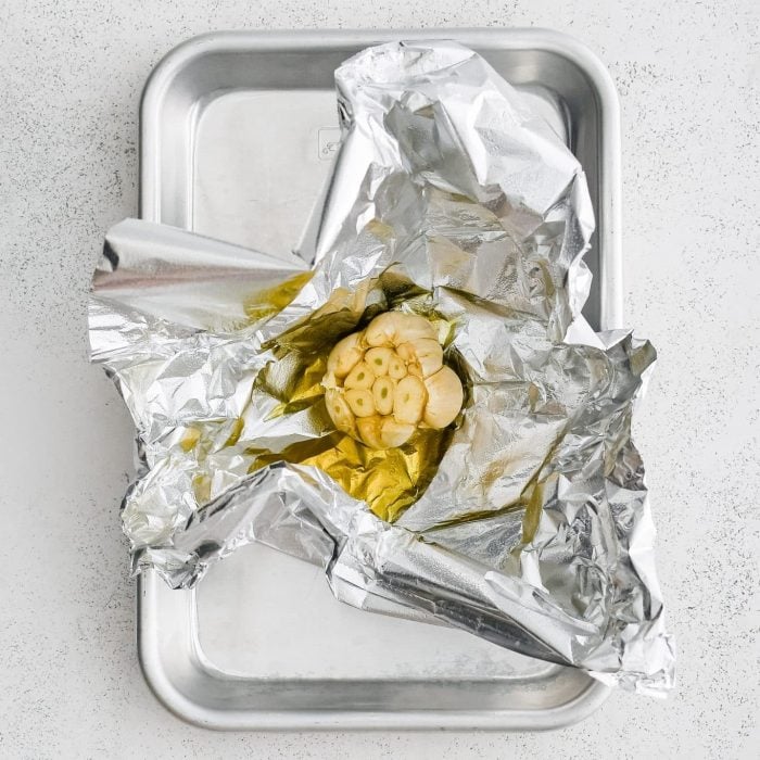 Whole garlic bulb on a piece of aluminum foil with the tip sliced off and drizzled with olive oil.