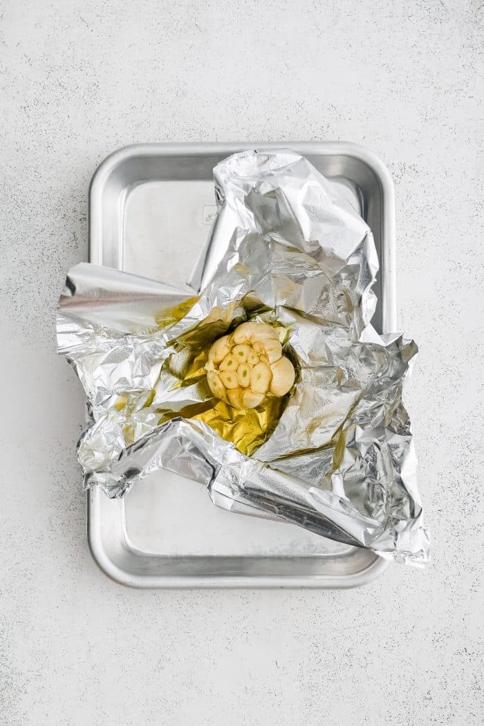 Whole garlic bulb on a piece of aluminum foil with the tip sliced off and drizzled with olive oil.