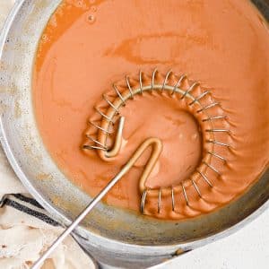 Sauce whisk set inside a skillet filled with dark brown roux.