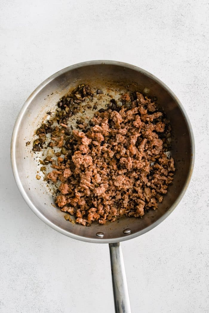 Fully cooked ground Italian sausage added to a large skillet filled with softened onions and chopped mushroom stems.