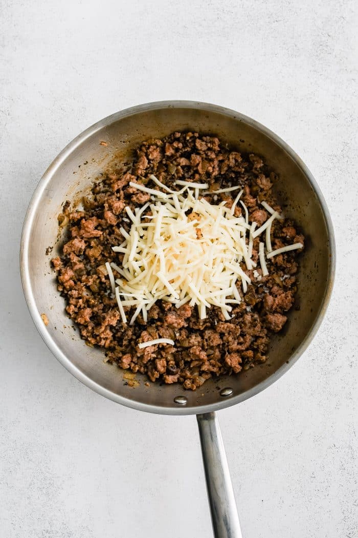 Shredded mozzarella cheese added to a large skillet filled with the sausage filling for stuffed mushrooms.