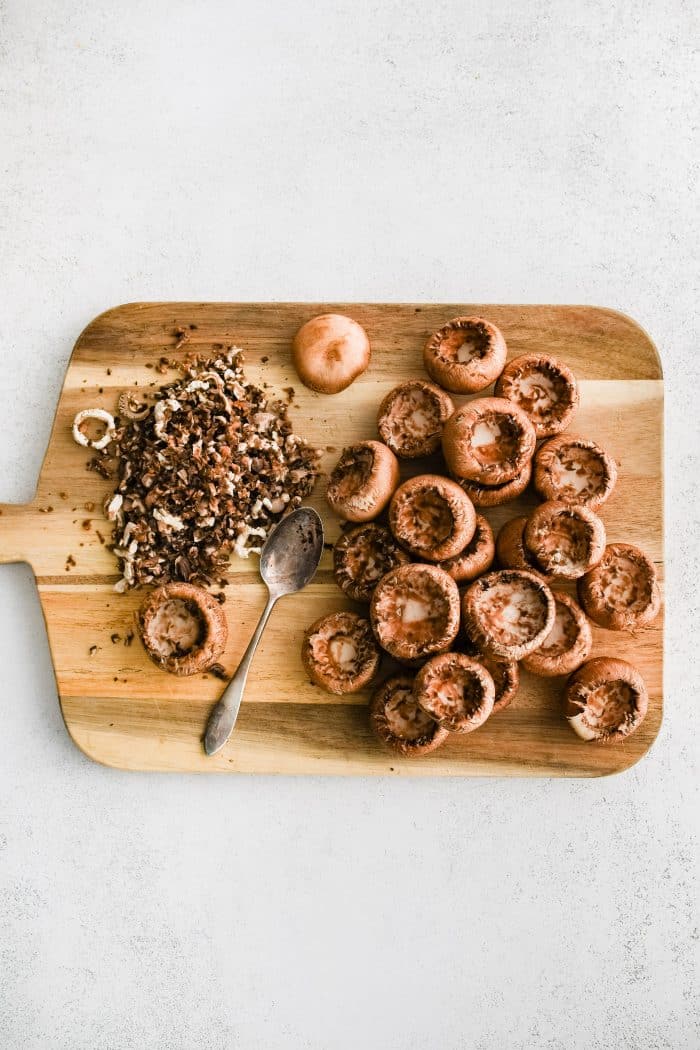 Large cutting board filled with baby Bella mushrooms with the gills scooped out.