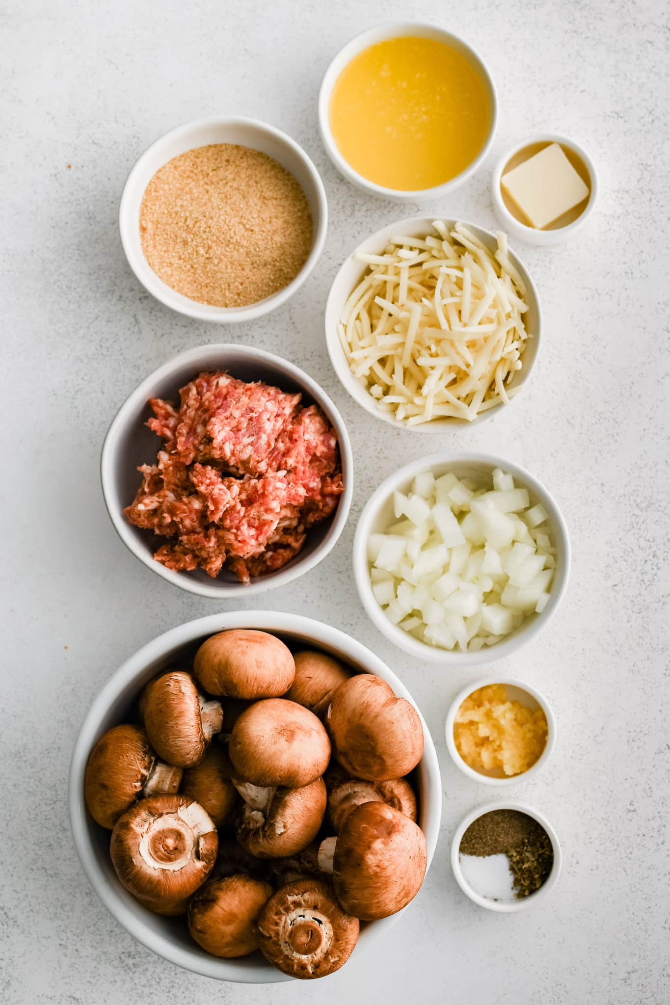All of the ingredients needed to make sausage stuffed mushrooms in individual measuring cups and ramekins.