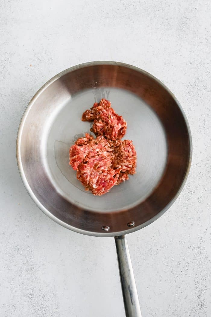 Raw ground Italian sausage in a large stainless steel skillet.