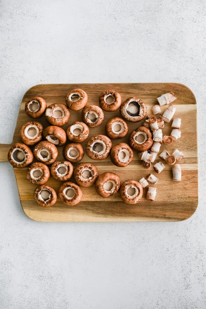 Large cutting board with baby Bella mushrooms with stems removed and set to the side.