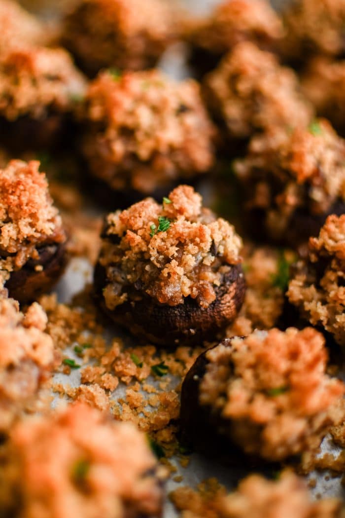 Close up image of sausage stuffed mushrooms on a baking sheet topped with crispy golden buttery breadcrumbs and garnished with fresh chopped parsley.