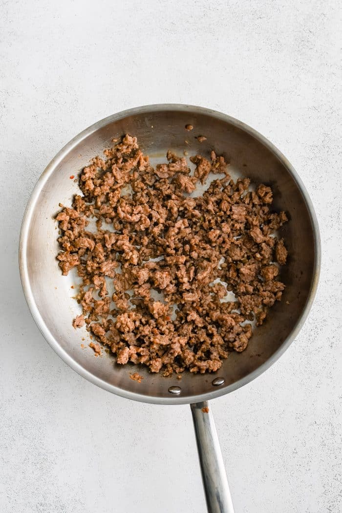 Large stainless steel skillet filled with cooked ground Italian sausage.